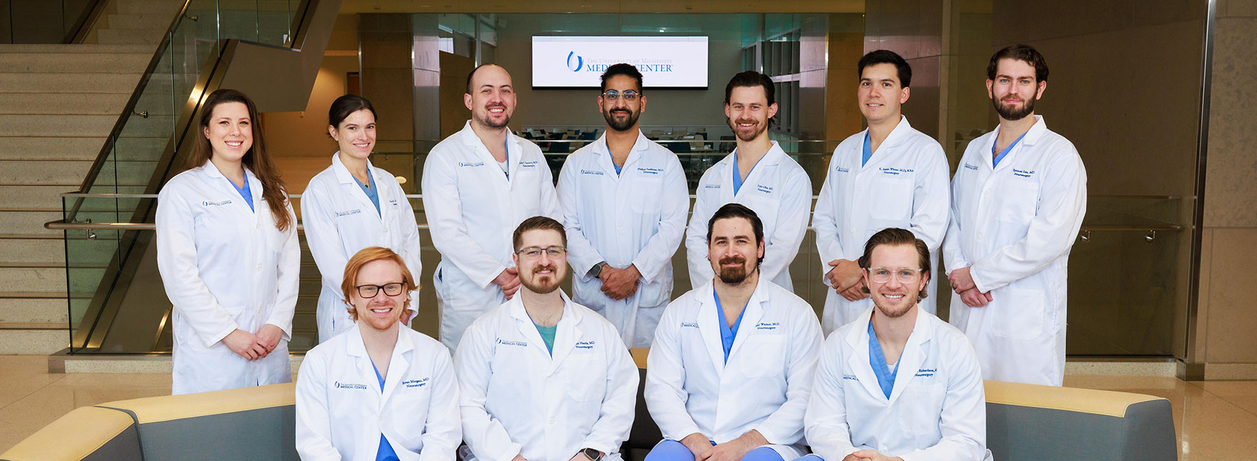 Eleven neurosurgical residents stand together for group photo wearing their white coats.